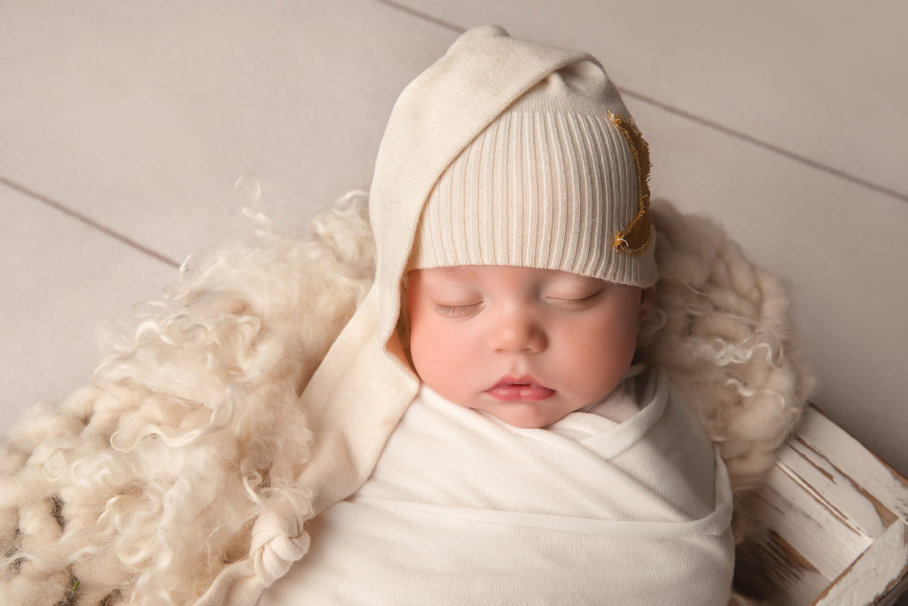 baby boy in white wrap and knit cap sleeps during Las Vegas Studio newborn portraits